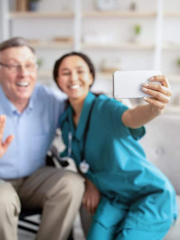 cheerful-disabled-senior-man-in-wheelchair-and-his-nurse-taking-selfie-indoors-selective-focus.jpg